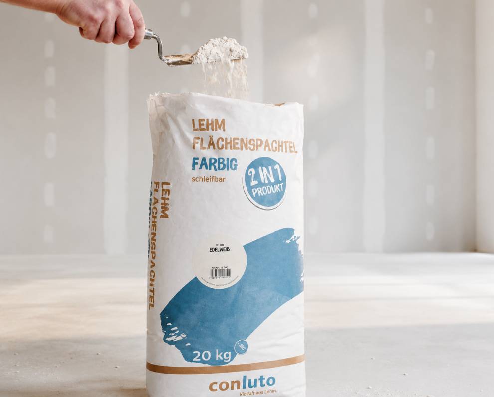 Hand entnimmt conluto Lehm-Flächenspachtel aus dem Sack
